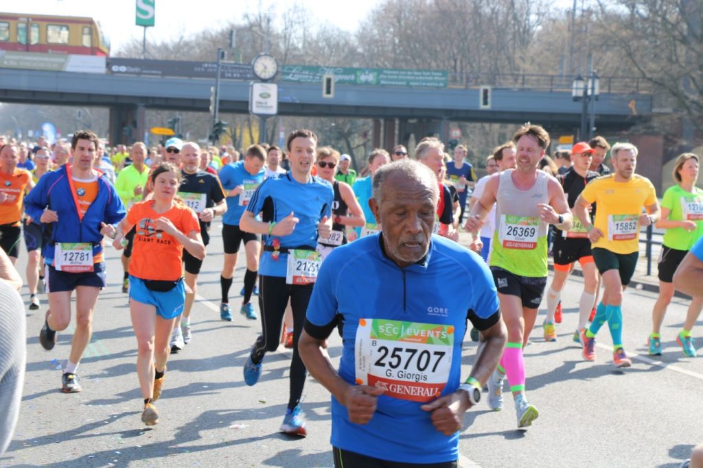 Em uma maratona, um senhor que aparenta ter uns 70 anos corre na frente de vários jovens.